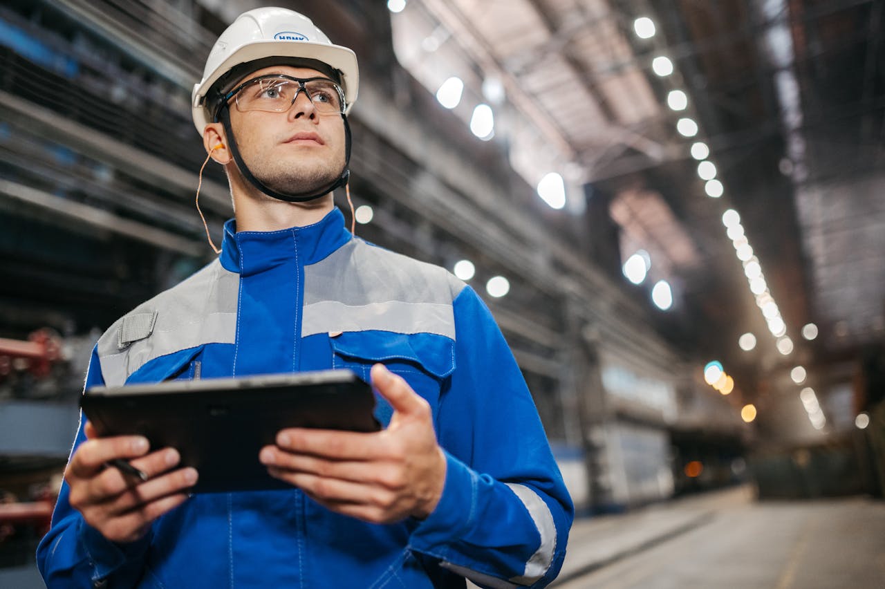services-03 Factory worker in safety gear using a tablet in a well-lit industrial setting.