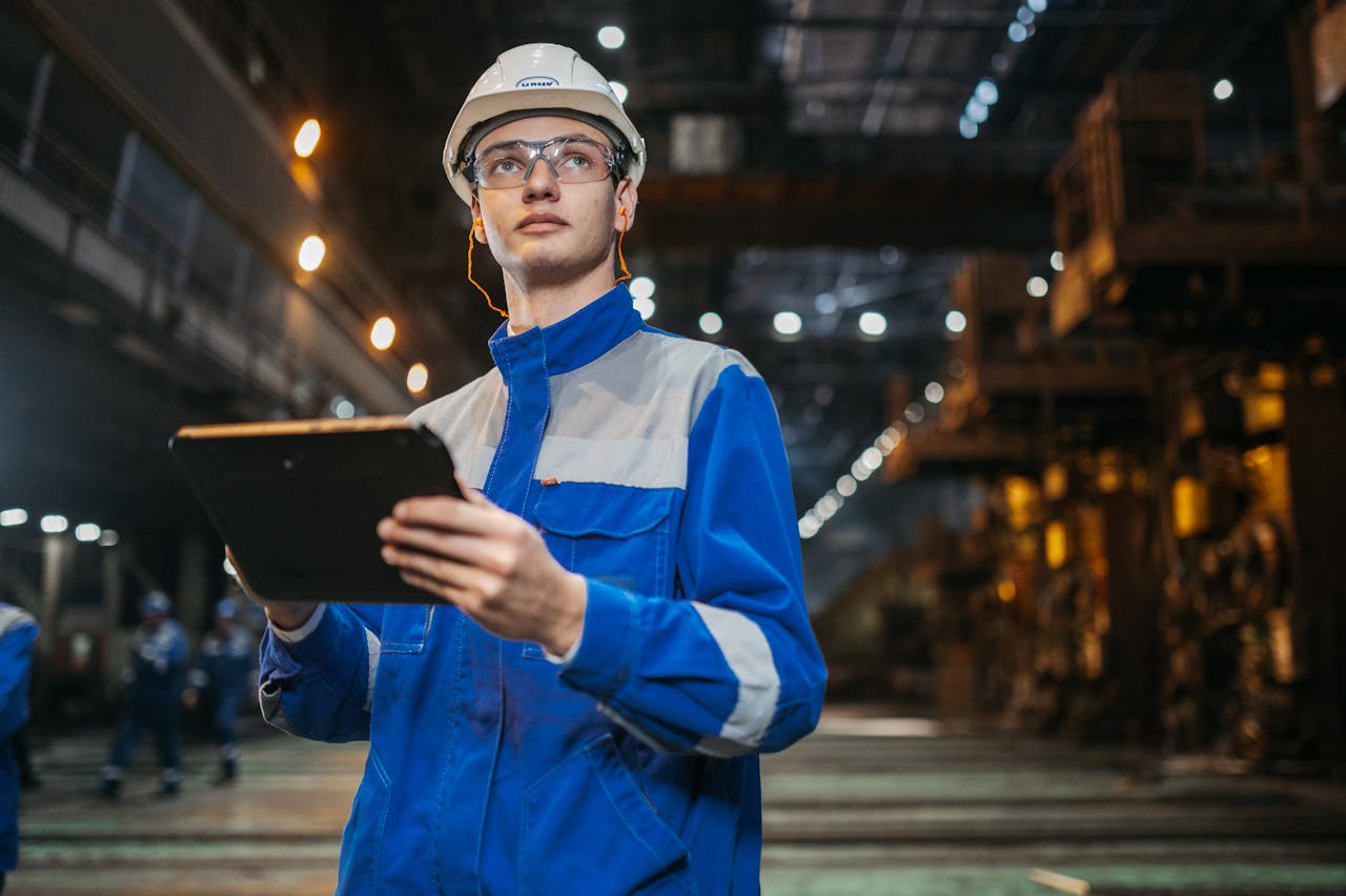 The Art of Drawing Readers In: Your attractive post title goes here Engineer in safety gear uses a tablet in a large industrial factory setting, focused and diligent.