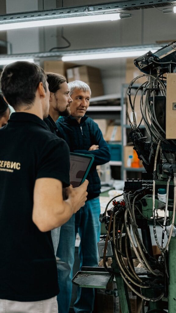 pexels photo 34054483 Three adults engaged in a discussion around complex machinery in a factory environment.