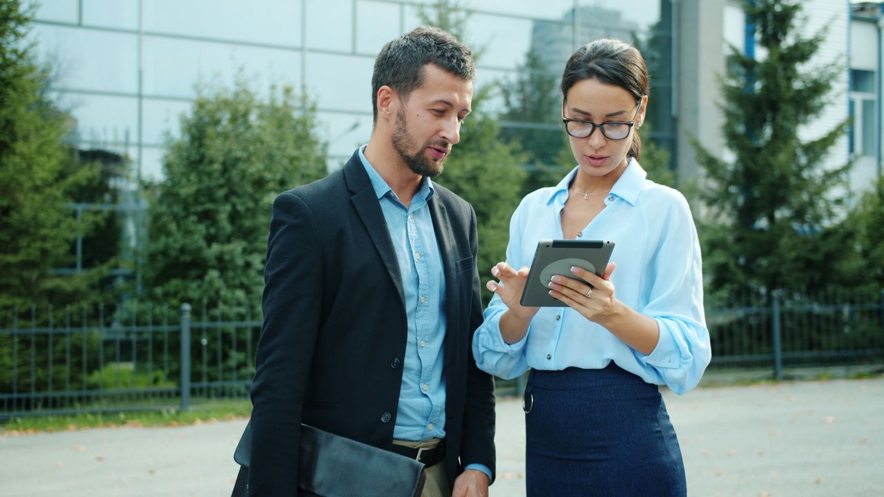 services-02 Professional colleagues discussing work on a tablet outdoors in an urban setting.