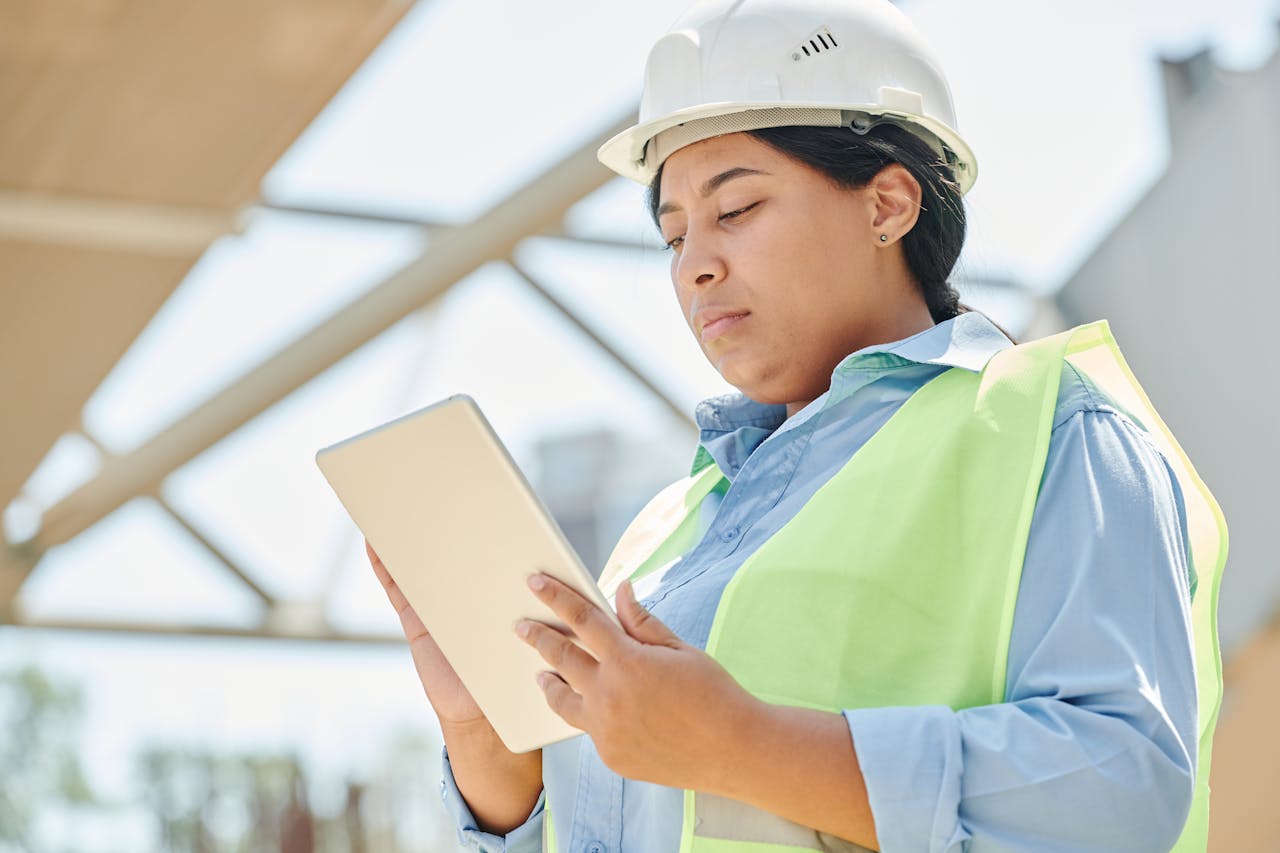 services-02 Confident female engineer in hard hat using a tablet computer at an outdoor construction site.